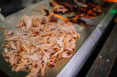 Shredded cooked meat on a metal tray, ready for serving. Background shows darker roasted pieces. Ideal for barbecue or food preparation themes. clipart