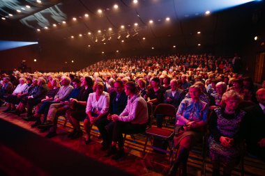 Valmiera, Letonya - 18 Kasım 2024 - Sahne ışıklarıyla aydınlatılmış loş bir oditoryumda oturan büyük bir seyirci, performans öncesi sıcak ve çekici bir atmosfer yaratıyor..