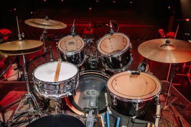 Valmiera, Letonya - 18 Kasım 2024 - Çanlar, tuzaklar ve mikrofonlarla donatılmış, boş bir konser salonunda canlı müzik gösterisi için hazır bir davul seti.
