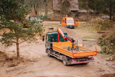 Valmiera, Letonya - 19 Kasım 2024 - Kırsal alanda kırmızı vinç, turuncu minibüs ve görünür inşaat malzemeleriyle donatılmış yeşil bir kamyoneti olan inşaat alanı.