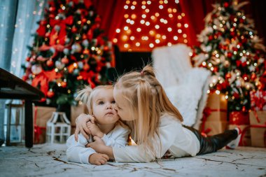 İki genç kardeş, ağaçlar, yanıp sönen ışıklar ve tatil süslemeleriyle çevrili, neşeli bir Noel ortamında iç açıcı bir anı paylaşıyorlar..