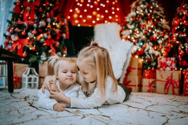 Noel ağaçları, ışıklar ve hediyelerle dolu bir ortamda yerde uzanan iki genç kardeş, bayramlarda sevgi dolu bir anı paylaşıyorlar..