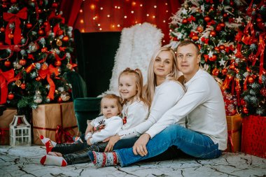 Güzel dekore edilmiş bir Noel ağacının yanında oturan bir çift. Etrafı şenlikli süsler, hediyeler ve hoş bir tatil dekoruyla çevrili..