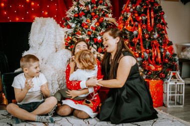 Neşeli bir aile, güzel dekore edilmiş bir Noel ağacının yanında gülüp oynuyorlar. Etrafı şenlikli süslemeler ve parlayan ışıklarla çevrili..