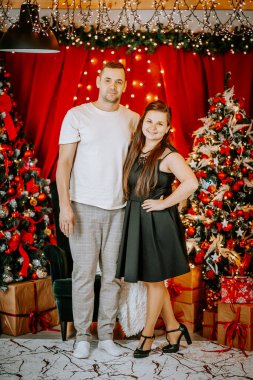 Parlayan Noel ışıklarının, süslenmiş ağaçların ve hediye paketlerinin önünde birlikte duran gülümseyen bir çift, bayram sezonunu kutluyor..