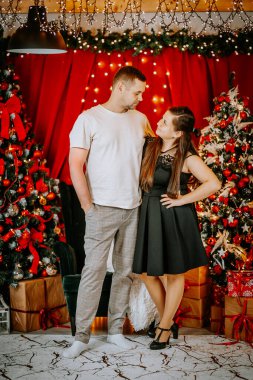 Sıcak bir Noel ortamında birlikte duran bir çift, süslü ağaçlar, parlayan ışıklar, ve paketlenmiş hediyeler, neşeli ve sevgi dolu bir anı paylaşıyorlar..
