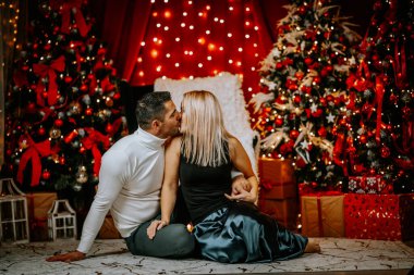 A couple shares a romantic kiss in a festive Christmas setting, surrounded by lit trees, wrapped gifts, and a cozy holiday atmosphere. clipart