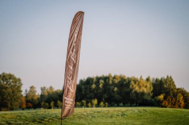 Valmiera, Letonya - 1 Eylül 2024 - Siyah Burner damgalı uzun bir tanıtım bayrağı ağaçlar ve açık mavi gökyüzü ile çevrili yemyeşil bir golf sahasında duruyor