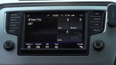 Valmiera, Letonya - 28 Kasım 2024 - Bağlı bir akıllı telefonu, iletişim seçeneklerini ve modern teknolojiyi vurgulayan bir SOS acil durum düğmesini gösteren bir araba bilgi işleme sistemi.