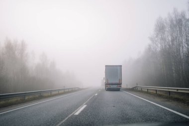 Sisli bir otoyolda ilerleyen bir kamyon çıplak ağaçlarla çevrili, düşük görüş mesafesi olan sakin ve gizemli bir atmosfer yaratıyor..