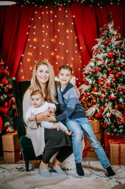 İki çocuğu olan bir anne, Noel ağacı, ışık ve paketlenmiş hediyelerle çevrili bir bayram ortamında birlikte oturur..