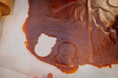 Close-up of brown dough with festive cookie cutouts, including a snow globe and bear shape, ready for holiday baking preparation. clipart