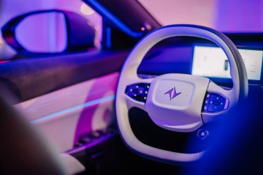 Riga, Letonya - 2 Aralık 2024 - Dongfeng T5 EVO modelinde direksiyona yakın çekim, parlak logosu, çok işlevli düğmeleri ve mor ve mavi tonlarda ortam aydınlatması.