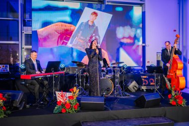 Riga, Letonya - 2 Aralık 2024 - Sahnede bir şarkıcı, klavyeci, davulcu ve basçıyla canlı performans sergiliyor..