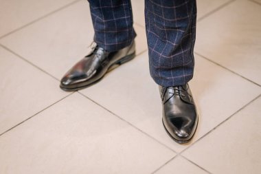 Kiremit döşeme üzerinde denizci ekoseli pantolonla eşleştirilmiş cilalı siyah deri ayakkabılardan oluşan yakın plan, resmi bir stil ve zarafet sergiliyor..
