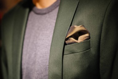 Close-up of a green blazer with a patterned pocket square, paired with a grey sweater, showcasing elegant and modern mens fashion clipart