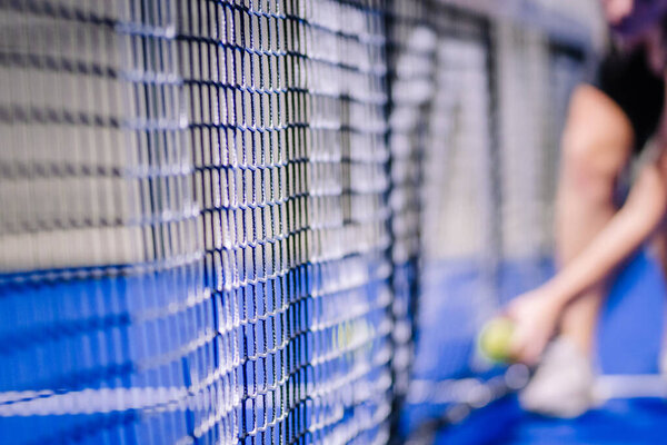 Рига, Латвия - 8 декабря 2024 года - Крупный план сетки падель корта с размытым игроком и мячом на заднем плане, подчеркивая нетто текстуру и напряжение. Падель.