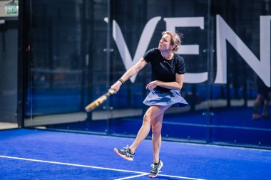 Riga, Letonya - 8 Aralık 2024 - Kadın bir padel oyuncusu, mavi kapalı bir padel kortunda topa vurmak için raketini sallıyor. Odaklanmış ve atletik performans. Padel sporu.