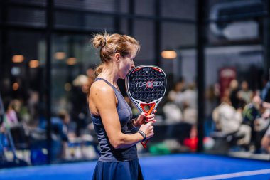 Riga, Letonya - 8 Aralık 2024 - HYDROGEN padel raketini kapalı bir sahada tutan kadın bir padel oyuncusu. Maça hazırlanıyor gibi görünüyor. Padel sporu