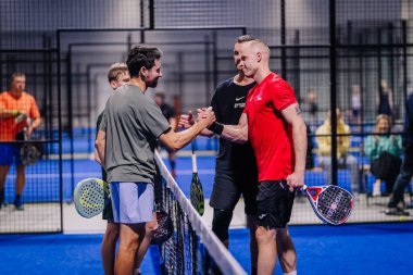 Riga, Letonya - 8 Aralık 2024 - Padel maçından sonra oyuncuların el sıkışması, raket tutması ve gülümsemesi, spor salonu arka planında.