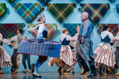 Valmiera, Letonya - 8 Aralık 2024 - Renkli geleneksel kostümlü Letonyalı halk dansçıları parlak ışıklar altında sahne alarak, senkronize hareketler yoluyla kültürel mirası sergilediler..