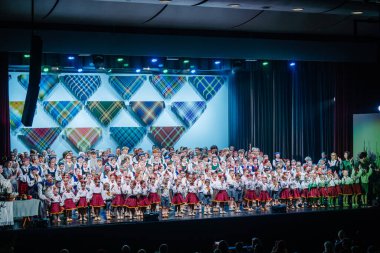 Valmiera, Letonya - 8 Aralık 2024 - Geleneksel Letonya Halk dansları kostümlü büyük bir grup çocuk ve yetişkin kültürel performans sırasında dekore edilmiş bir sahnede duruyor.