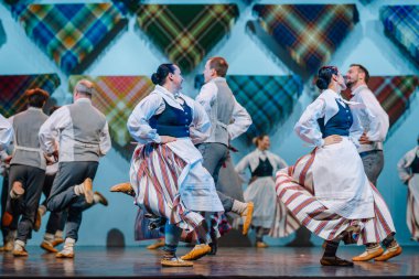 Valmiera, Letonya - 8 Aralık 2024 - Renkli geleneksel kostümlü Letonyalı halk dansçıları parlak ışıklar altında sahne alarak, senkronize hareketler yoluyla kültürel mirası sergilediler..