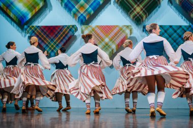Valmiera, Letonya - 8 Aralık 2024 Letonyalı halk dansçıları sahnede donanma yelekleriyle geleneksel beyaz ve çizgili etek giyip senkronize hareketlerde zarifçe döndüler..