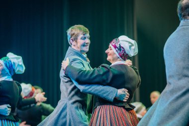 Valmiera, Letonya - 8 Aralık 2024 - Bir çift Letonya Halk Dansı yapıyor, geleneksel Letonya kıyafetleri giyiyorlar, sahnede kültürel bir gösteri sırasında neşeli ifadeler takınıyorlar..