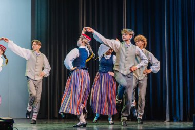 Valmiera, Letonya - 8 Aralık 2024 - Geleneksel Letonya kostümlü bir grup dansçı renkli dekorasyon ve ışıklarla Letonya Halk Dansını sahnelerken.