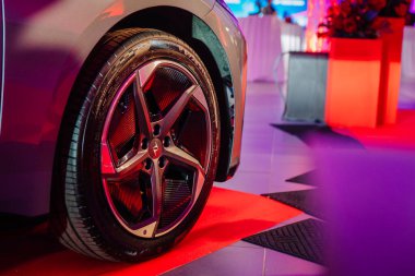 Riga, Letonya - 2 Aralık 2024 - Dongfeng marka lüks bir araba tekerleğinin yakın çekimi kırmızı halı üzerinde parlak ışık ve dekorlu bir iç mekanda.