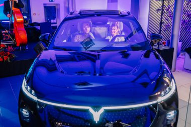 Riga, Letonya - 2 Aralık 2024 - Pürüzsüz bir Dongfeng elektrikli arabası içinde iki kişi oturuyor, ön camdan bakılıyor, parlak ışıklandırmalı lüks bir etkinlikte.