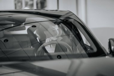 Riga, Letonya - 2 Aralık 2024 - Dongfeng arabasında oturan bir kadın, siyah-beyaz, yansıtıcı bir ön camı ve modern bir ortamda düşünceli bir ifadeyle yakalandı..