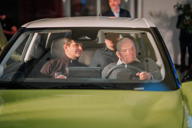 Riga, Letonya - 2 Aralık 2024 Bir Dongfeng arabasında oturan üç adam, birinin elinde bir kadeh şarap, canlı bir aydınlatma ve modern bir otomotiv iç mekanı olan.