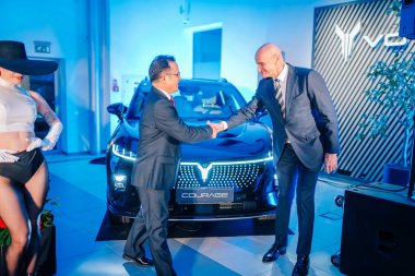 Riga, Latvia - December 2, 2024 - Executives shaking hands in front of a sleek Dongfeng Courage car at a launch event, showcasing professionalism and modern automotive design clipart