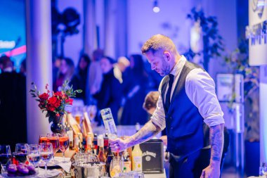 Riga, Letonya - 2 Aralık 2024 - Bir barmen bir Dongfeng etkinliğinde bardaklar, şişeler ve çiçeklerle çevrili bir kokteyl hazırlıyor..