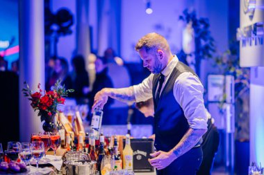 Riga, Letonya - 2 Aralık 2024 - Bir barmen canlı mavi ışıklandırma altında bir Dongfeng etkinliğinde içki hazırlar..