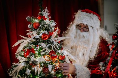 Noel Baba bir Noel ağacını şenlikli süsler, yaylar ve renkli güneş gözlükleriyle süsler ve tuhaf bir tatil sahnesi yaratır..