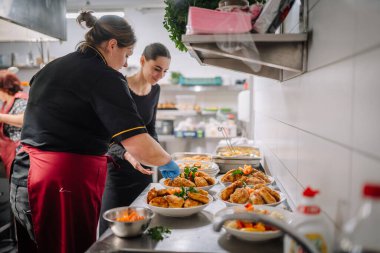 Valmiera, Latvia - December 13, 2024 -  Professional chefs plating fried chicken dishes in a commercial kitchen, with fresh vegetables and garnish. No logos visible. clipart