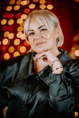 Close-up portrait of a confident woman with blonde hair posing against a festive red background with golden bokeh lights. clipart