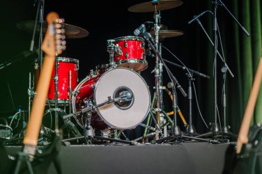 Close-up of a red drum set on stage with microphones, cymbals, and other musical equipment prepared for a live performance or concert. clipart