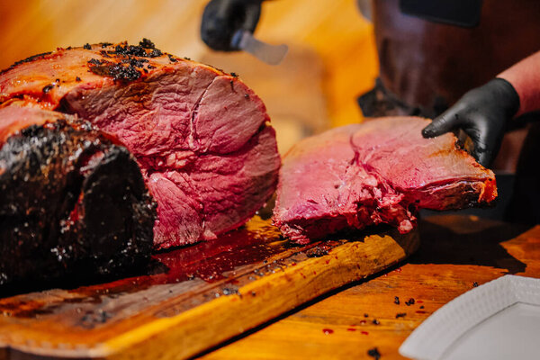Valmiera, Latvia - December 7, 2024 - A close-up of freshly sliced, juicy roasted meat on a wooden cutting board, with a chefs gloved hands and carving knife in view
