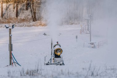 A snow cannon producing artificial snow on a snowy slope, surrounded by a winter landscape, with frost and mist in the air. clipart