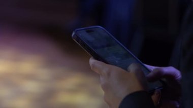 Valmiera, Letonya - 18 Ekim 2024 - Kopya alanı için bulanık bir arkaplanı olan loş ışıklı bir ortamda akıllı telefonu tutan ellerin yakın çekimi.