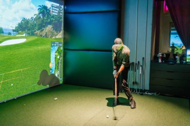 Riga, Letonya - 8 Ocak 2024 - Bir golfçü, gelişmiş golf analitiği sergilenen ekranda sanal bir kursla kapalı bir golf simülatöründe sallanıyor.