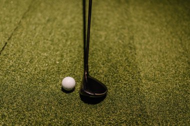 Riga, Letonya - 8 Ocak 2024 - Yapay çim üzerine kurulmuş bir golf topu ve sopasıyla yakın plan temiz ve minimalist bir kompozisyona odaklanmış bir çekim için hazır..