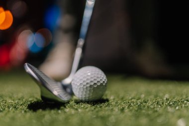 Riga, Letonya - 8 Ocak 2024 - Suni sahada bir golf topu ve sopasının yakın çekimi, arka planda bulanık bokeh aydınlatma, kapalı bir golf sahasında çekim için hazır..