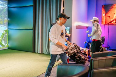 Riga, Letonya - 8 Ocak 2024 - Arka planda bir Trackman simülatörü ve golf ekipmanı olan kapalı bir golf tesisinde golf eldiveni tutan bir kişi.