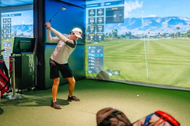 Riga, Letonya - 8 Ocak 2024 - Bir golfçü kapalı alanda Trackman simülatörü kullanıyor, salıncağın ortasında, sanal bir golf sahası ve ekranda ayrıntılı performans ölçümleri gösteriliyor.