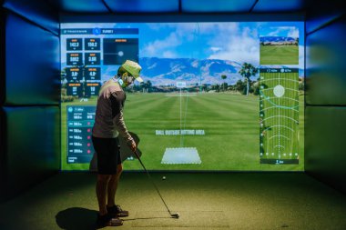 Riga, Letonya - 8 Ocak 2024 Spor giyimli bir adam, kapalı bir simülatörde golf oynuyor, ekranda sanal golf sahası ve detaylı performans verileri var..